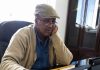 Somaliland: A Local War or a Wider Geopolitical Struggle? Engineer Abdi Ali Barkhad seated at his office desk, wearing a tan cap, glasses, beige cardigan, and blue shirt.