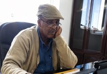 Somaliland: A Local War or a Wider Geopolitical Struggle? Engineer Abdi Ali Barkhad seated at his office desk, wearing a tan cap, glasses, beige cardigan, and blue shirt.